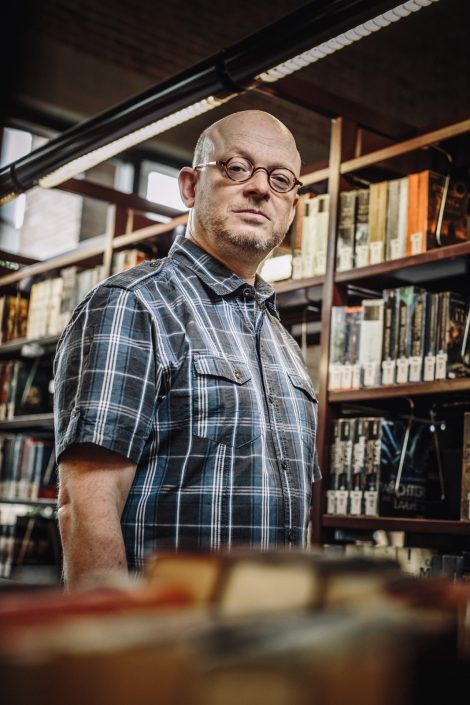 Timur Vermez blickt in die Kamera. Er steht zwischen Bücherregalen der Münchner Stadtbücherei.